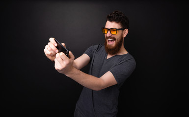 Excited bearded man  playing on smartphone over dark gray background