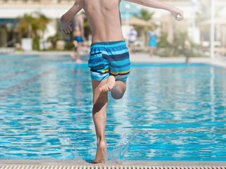Boy taking off to jump into swimming pool. Back view.