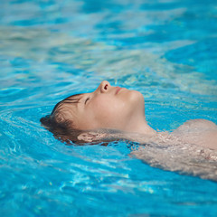 Cute European boy swimming backstroke in the pool.