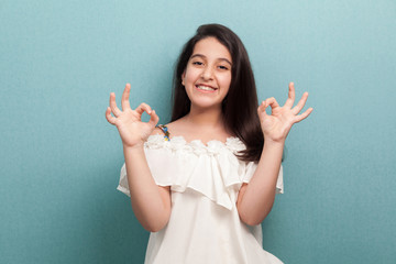 Portrait of happy beautiful brunette young girl with long straight hair in white dress standing...