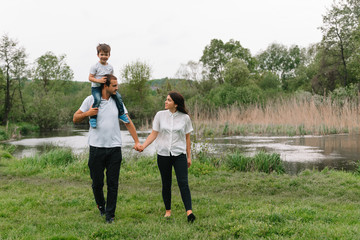 Fototapeta premium Happy family: mother father and child son on nature on sunset. Mom, Dad and kid laughing and hugging, enjoying nature outside. Sunny day, good mood. concept of a happy family