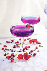 Thai asian purple Anchan tea in cocktail glasses with dry rosebuds and blue tea, tea leaves and green basil leaves, healthy organic detox Asian herbal tea clitoria Butterfly Pea on marble background