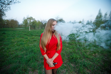 Vape woman. Young beautiful blonde girl in red dress and sunglasses smokes an electronic cigarette...