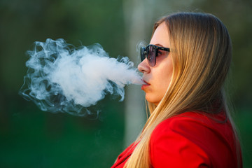 Vape woman. Young beautiful blonde girl in red dress and sunglasses smokes an electronic cigarette...