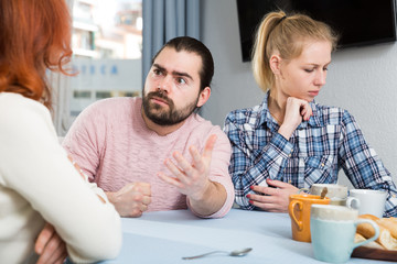 Family of three sitting together with cup of tea at table at home