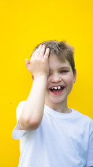 shy boy smilling. hand closes face. laugh with theeth. vertical view on yellow background.