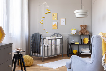 Bee decorations in a kid room interior with a crib, armchair and teddy bear. Real photo