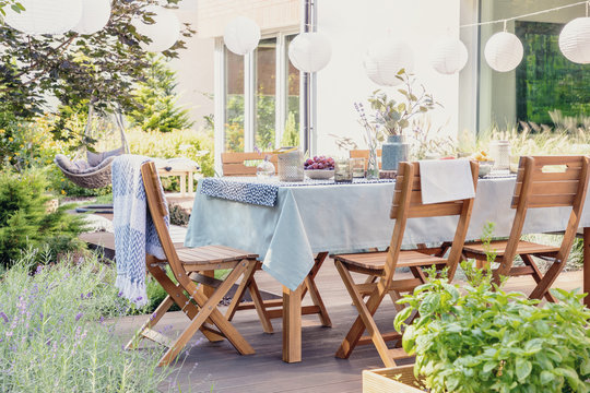 Wooden chairs at table with flowers and food in the garden with plants and lanterns. Real photo