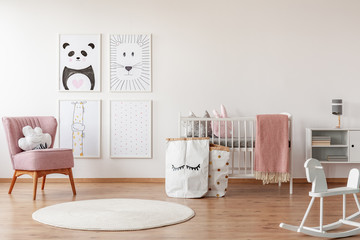 Rocking horse and pink chair in child's room interior with posters, white rug and cradle. Real photo