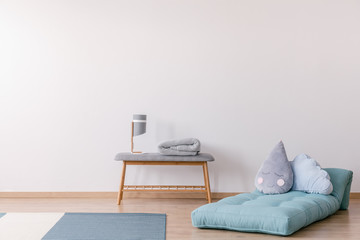 Pillows on blue mattress next to bench with lamp in white simple kid's bedroom interior. Real photo