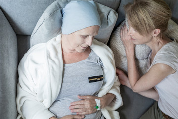 Blonde daughter and ill and sad mother laying in bed together. Home cancer treatment concept