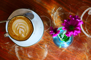 Coffee cup with cappuccino and flowers in bottle on the worn polished tabletop top view
