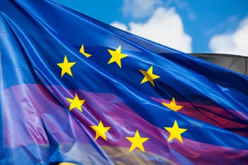 Fototapeten Waving Flag of the European Union in Foreground, Flag of Germany seen through © christianthiel.net