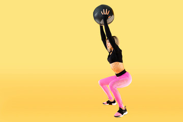 Fototapeta na wymiar Strong woman workout with med ball. Photo of sporty latin woman in fashionable sportswear on yellow background. Strength and motivation.
