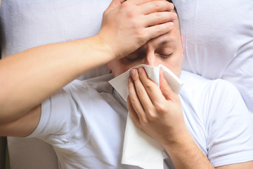 Sick desperate man has flu. Rhinitis, cold, sickness, allergy concept. Pretty sick man has runnning nose, rubs nose with handkerchief. Sneezing male. sneezing in a tissue