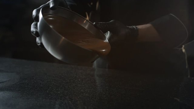 Chocolatier pours melted chocolate from the bowl to the cold table for tempering, making of sweets and handmade chocolate candies, 4k UHD Prores HQ 422