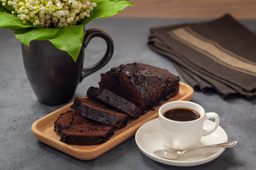 Ciasto czekoladowe na drewnianej tacce, kawa, konwalie i ścierka kuchenna