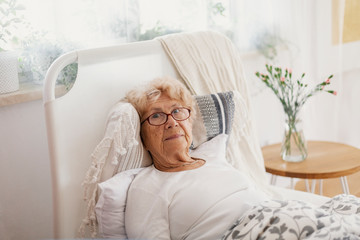 Sick senior woman with glasses lying in hospital bed