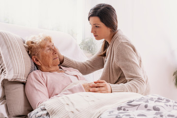 Young daughter supporting sick mother lying in hospital bed