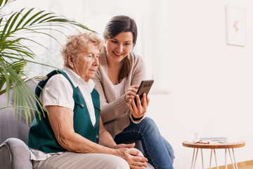 Senior woman in nursing home with her granddaughter showing her how to use a mobile phone