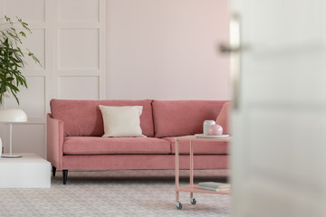 Open door to fashionable living room with white wall and pastel pink settee