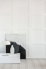 White lamp, and white and black vases on platform in simple interior