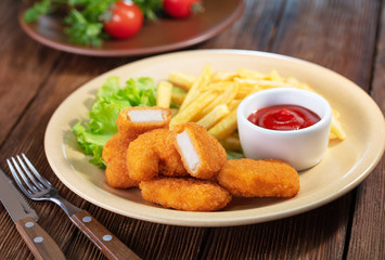 fried chicken with french fries and vegetables on wooden table