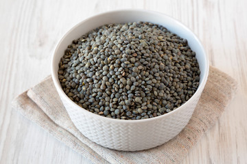 Dry green french lentils in a bowl over white wooden background, side view.