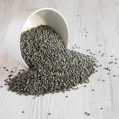 Green french lentils in a bowl over white wooden surface, side view. Close-up.