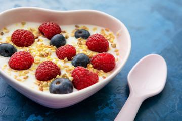 Healthy Morning Yogurt Berries Breakfast Side View. Ceramic Spoon near Yoghurt with Seeds, Raspberry and Blackberry in Bowl on Blue Table. Closeup Homemade Creamy Diet Dish for Wellness and Good Mood