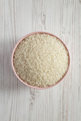 Dry white rice basmati in a pink bowl over white wooden surface, top view. Flat lay, overhead, from above. Close-up.