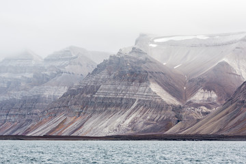 Billon year old jagged rock formations with different green moss and snow within, Svalbard,...