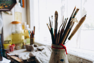 Artist's tools, brushes, paints and a palette lie on a old white wooden sills near light window background. Copy space for text