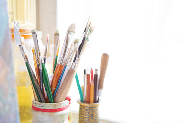 Artist's tools, brushes, paints and a palette lie on a old white wooden sills near light window background. Copy space for text