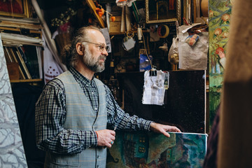 Fototapeta na wymiar 01.04.2019 Kyiv, Ukraine: stylish man with a gray beard and long hair dressed in a shirt and the jaillet communicates with the student in his little art studio