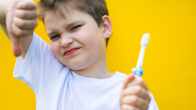 sad boy showing blurred dislike and thooth brush. focus on face. dental hygiene, dentist scared, no brushing teeth concept