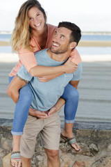 man giving his girlfriend a piggy back on the beach
