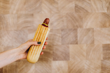 French hot dog in a bacon with fried sausage in a woman's hand against the wall