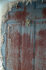 The grungy dilapitaed exterior door with ornate door knocker is an uninviting sight. Maintenance work is needed to remove the peeling paint.