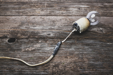 Retro lightbulb with damaged wires, vintage wooden background with space for text. Concept -...