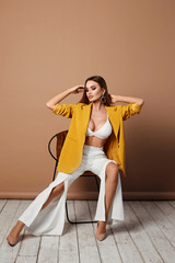 Beautiful sexy and fashionable blonde girl with a perfect body, with big bustin stylish yellow blazer sits on the chair indoors