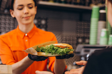 young beautiful brunette girl selling, cook and waiter in a cafe catering facility gives the buyer...