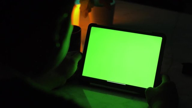 Over the shoulder view of asian man using tablet computer . Green screen of technology being used. Chroma Key tablet.