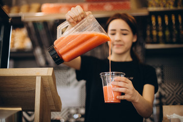 drink made from red summer fruits and berries in a blender. The process of pouring the finished smoothie into a glass in hand of girl on a natural green background