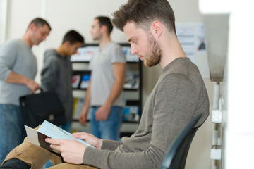 young man reading a magazine while waiting in office