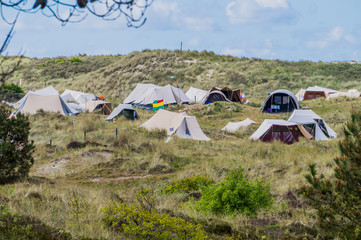 Typical Dutch Vlieland island tent camp of hippies amid of dunes and shrub vegetation with flags waving