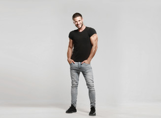 Muscular model sports young man in grey jeans and black t-shirt on a grey background. Fashion...