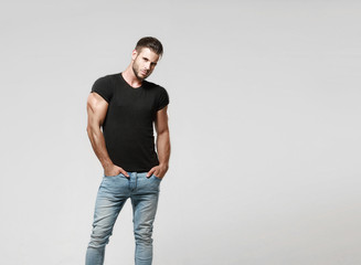 Muscular model sports young man in jeans and black t-shirt on a grey background. Fashion portrait...