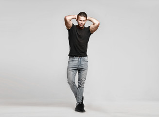 Muscular model sports young man in jeans and black t-shirt on a grey background. Fashion portrait of brutal sporty healthy strong muscle guy with a modern trendy hairstyle.