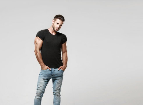 Muscular model sports young man in jeans and black t-shirt on a grey background. Fashion portrait of brutal sporty healthy strong muscle guy with a modern trendy hairstyle.